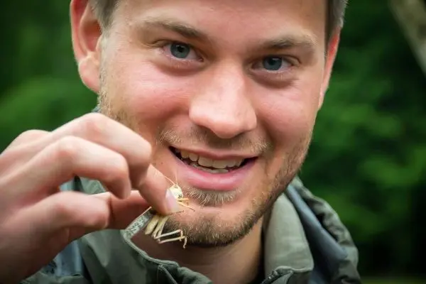 Mann hält eine Heuschrecke in der Hand und lächelt