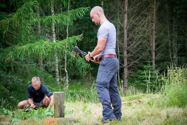 Mann mit Axt schlägt auf einen Holzblock, während ein anderer Mann im Hintergrund arbeitet