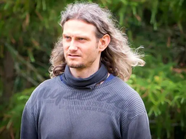 Mann mit langen Haaren trägt einen schwarzen Pullover und schaut nachdenklich