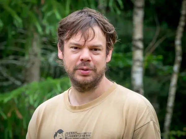 Mann mit unordentlichem Haar steht vor grüner Vegetation