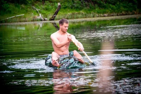 Mann paddelt auf improvisiertem Boot im Wasser