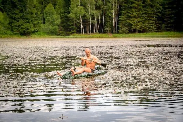 Mann paddelt auf improvisiertem Floß durch einen See mit Wasserpflanzen