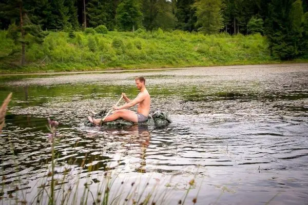 Mann paddelt auf improvisiertem Floß über einen ruhigen See