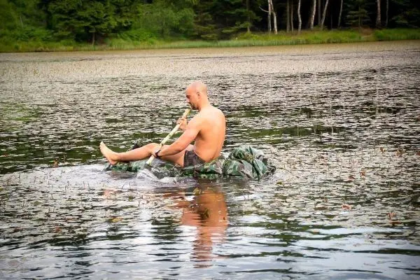 Mann paddelt auf improvisierter Schwimmkonstruktion aus Tuch im Gewässer