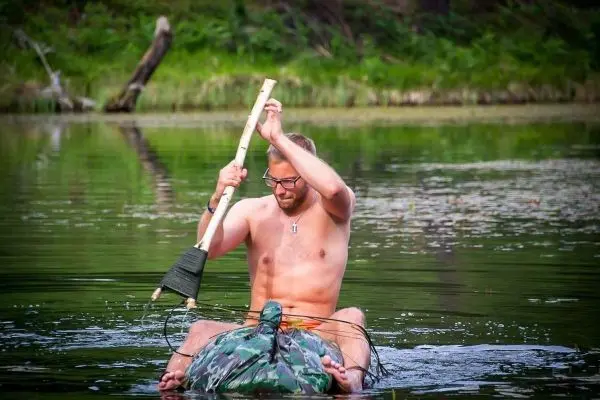 Mann paddelt mit einem Stock auf einem camouflagefarbenen Boot im Wasser