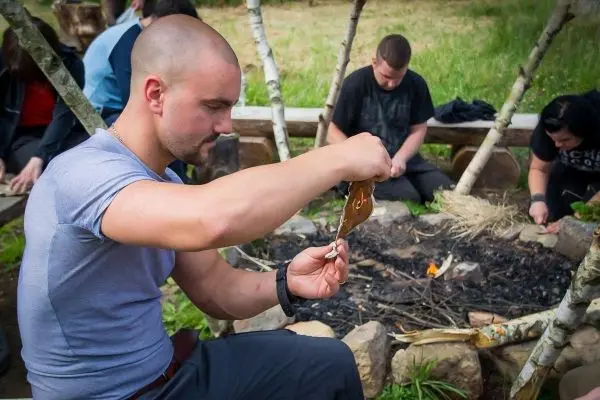 Mann schneidet Zunder neben einem kleinen Feuer im Freien