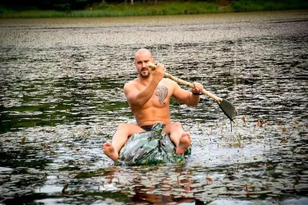 Mann sitzt auf einem improvisierten Floß und hält ein Paddel in der Hand