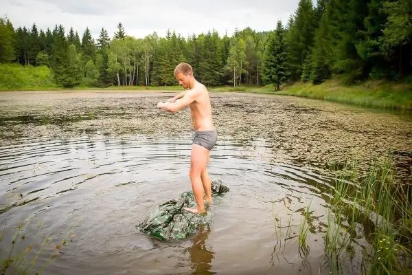 Mann steht auf einem camouflagefarbenen Tuch im Wasser eines Teiches