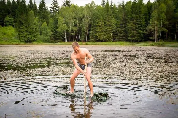 Mann steht auf einer camouflagefarbenen Unterlage im Wasser und sticht mit einem Stock