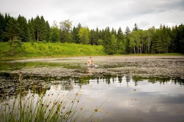 Mann steht im Wasser eines ruhigen Sees, umgeben von Pflanzen und Bäumen