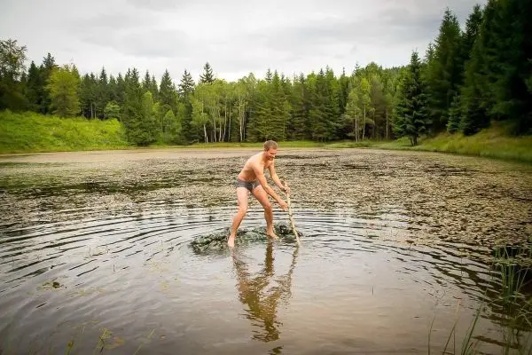 Mann steht im Wasser und hält einen Stock, um das Ufer zu erreichen