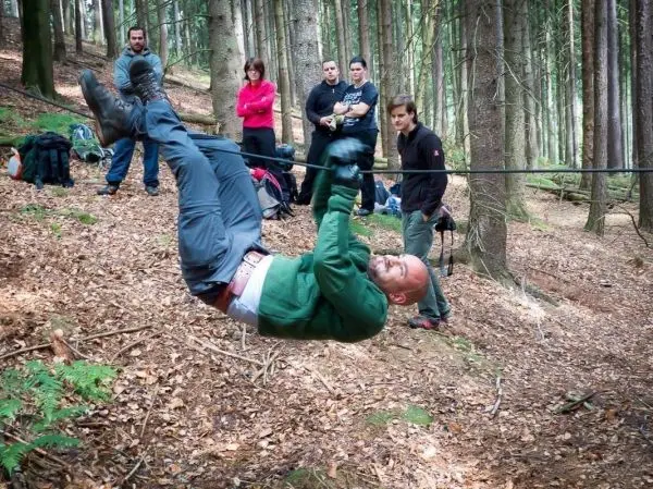 Mann überquert selbstgebaute Seilbrücke im Wald, Zuschauer beobachten