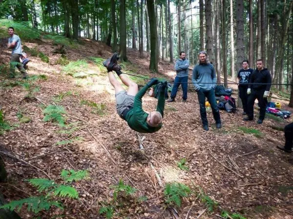 Mann überquert selbstgebaute Seilbrücke im Wald, Zuschauer beobachten