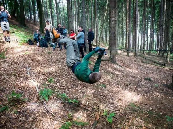Mann überquert selbstgebaute Seilbrücke im Wald, Zuschauer beobachten