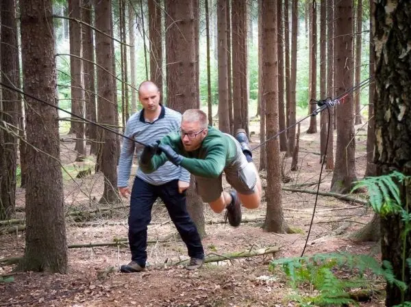 Mann überquert selbstgebaute Seilbrücke zwischen Bäumen im Wald