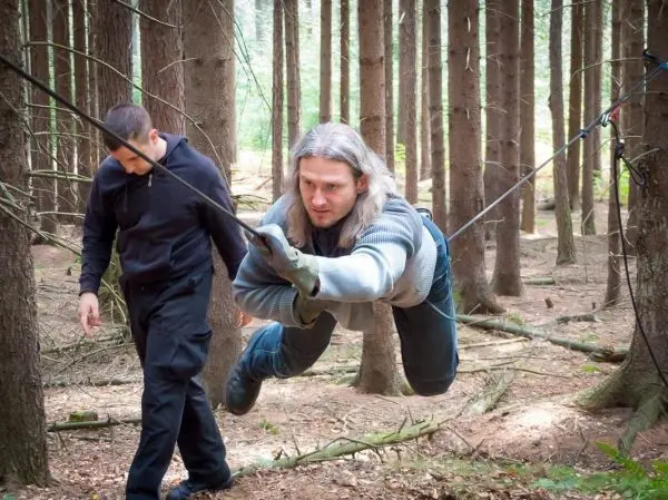Mann überquert selbstgebaute Seilbrücke zwischen Bäumen im Wald