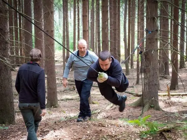 Mann überquert selbstgebaute Seilbrücke zwischen Bäumen im Wald