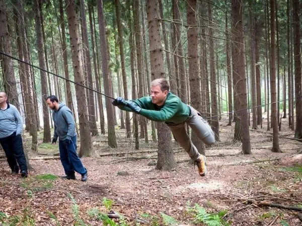 Mann überquert selbstgebaute Seilbrücke zwischen Bäumen im Wald