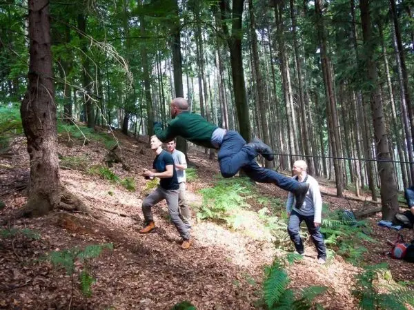 Mann überquert selbstgebaute Seilbrücke zwischen Bäumen im Wald