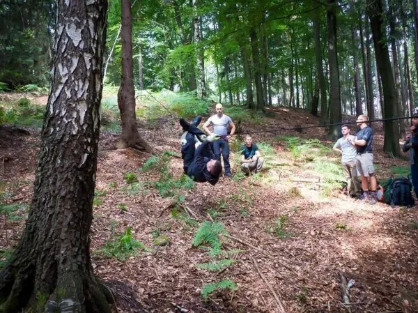 Mann überquert selbstgebaute Seilbrücke zwischen Bäumen, Zuschauer beobachten