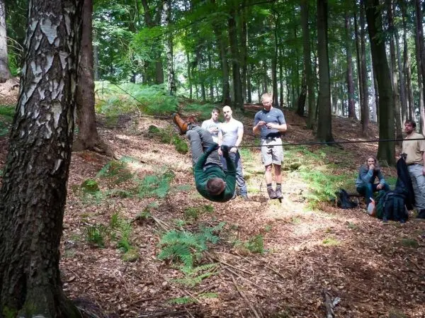Mann überquert selbstgebaute Seilbrücke zwischen zwei Bäumen im Wald