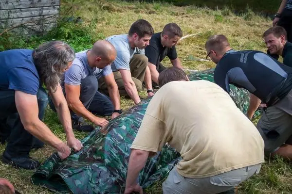 Mehrere Personen heben eine camouflagefarbene Plane gemeinsam an
