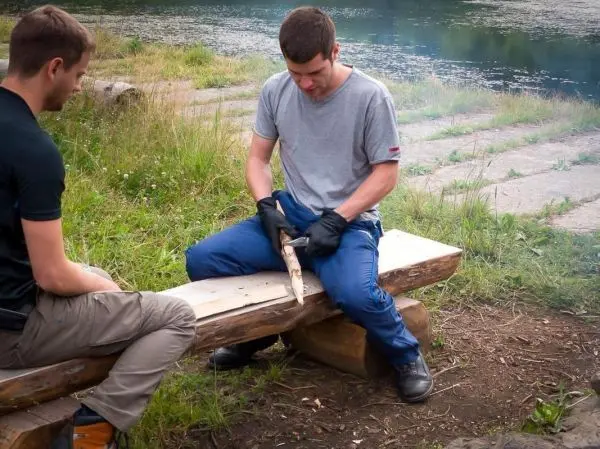 Messer bearbeitet Holzstück auf einer Bank am Wasser