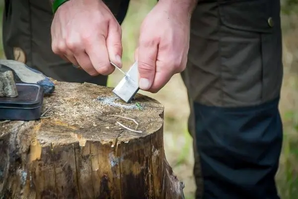 Person bearbeitet Holz mit einem Werkzeug auf einem Baumstumpf beim Survival Training