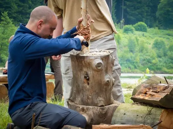 Person bearbeitet Holz mit einem Werkzeug beim Überlebenstraining