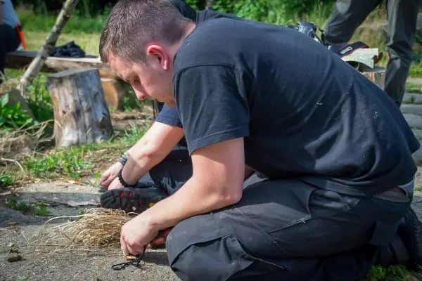 Person bereitet Zunder auf dem Boden vor beim Survival Training