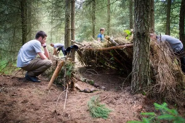Person betrachtet selbstgebaute Unterkunft im Wald beim Überlebenstraining