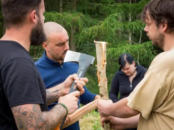 Person hält Axt, während andere Personen Holz bearbeiten beim Survival Training