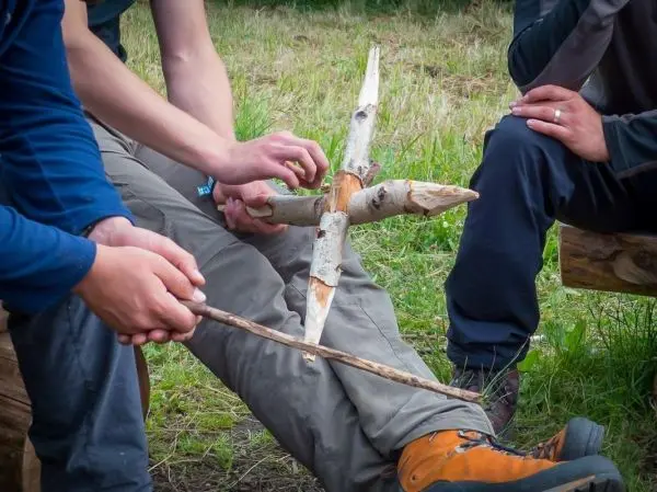 Person hält einen Stock und arbeitet an einer Holzstruktur beim Überlebenstraining