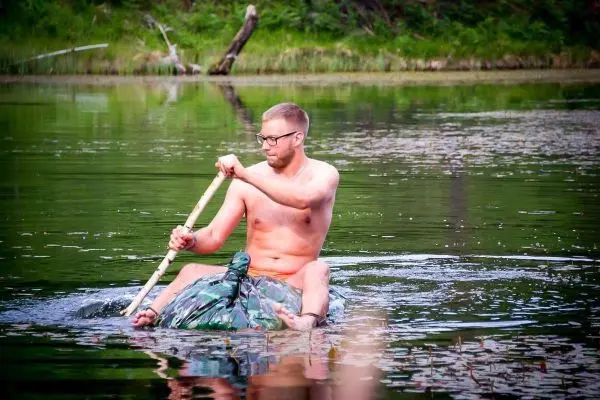 Person paddelt auf einem selbstgebauten Floß im Wasser