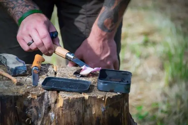 Person schneidet mit einem Messer auf einem Baumstumpf