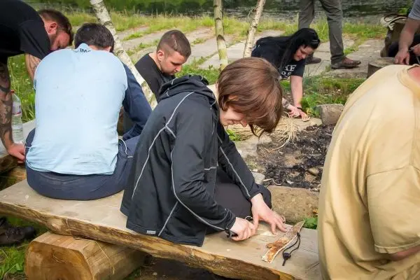 Person schnitzt mit einem Messer auf einem Holzblock beim Überlebenstraining
