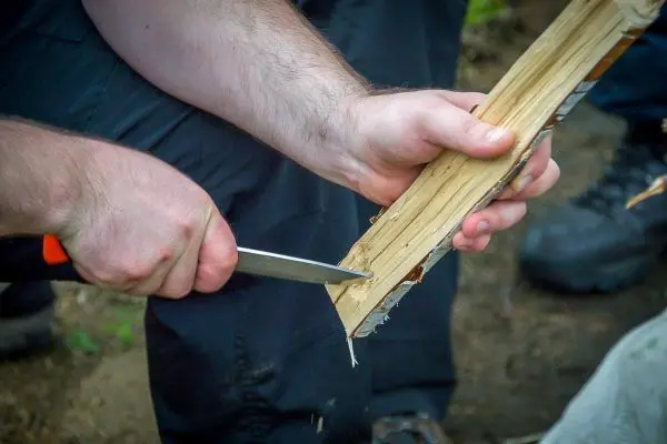 Person schnitzt mit einem Messer in einen Holzstock beim Überlebenstraining