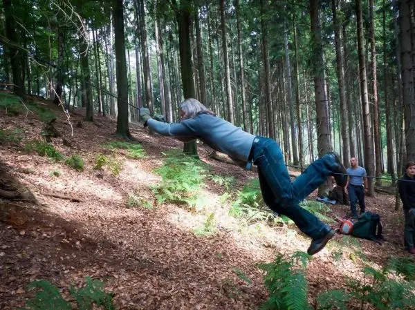 Person schwingt an einem Seil zwischen Bäumen im Wald