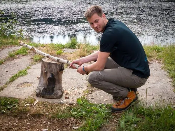 Person sitzt auf dem Boden und bearbeitet einen Baumstumpf mit einem Stock