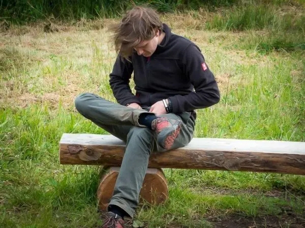 Person sitzt auf einem Holzstamm und zieht eine Hose an