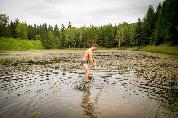 Person steht auf einem Stein im Wasser und hält einen Stock