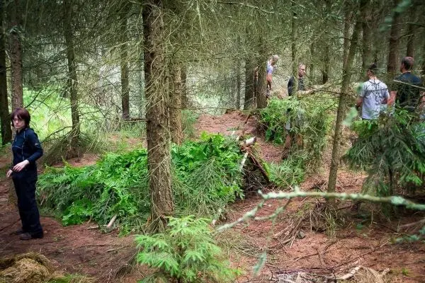 Person steht neben einer selbstgebauten Unterkunft im Wald