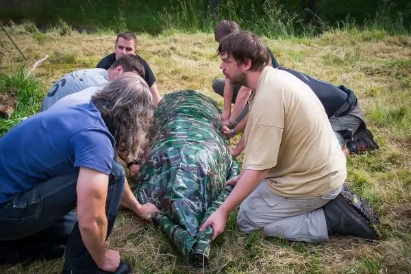 Sechs Personen tragen eine improvisierte Trage mit camouflagefarbenem Material