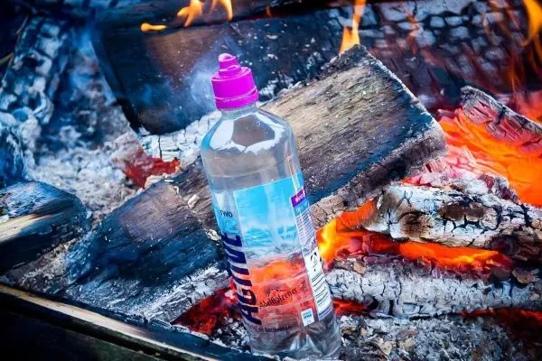 Wasserflasche steht zwischen brennenden Holzscheiten im Feuer