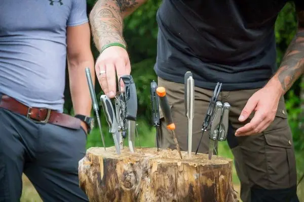 Werkzeug wird in einen Baumstumpf gesteckt, mehrere Messer und Werkzeuge sichtbar