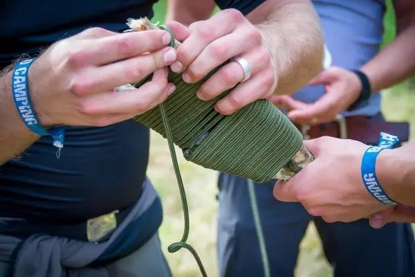 Zwei Hände wickeln Paracord um einen Stock zur Stabilisierung