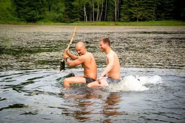 Zwei Männer sitzen auf einem improvisierten Floß und paddeln mit einem Stock im Wasser