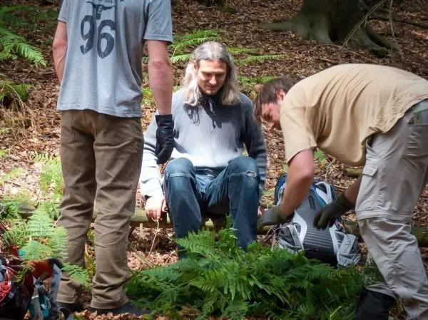 Zwei Personen arbeiten am Boden, während eine dritte Person auf einem Baumstamm sitzt