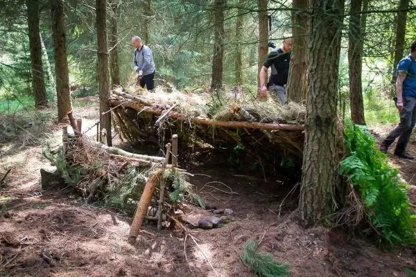 Zwei Personen arbeiten an einer selbstgebauten Tarp-Notunterkunft im Wald