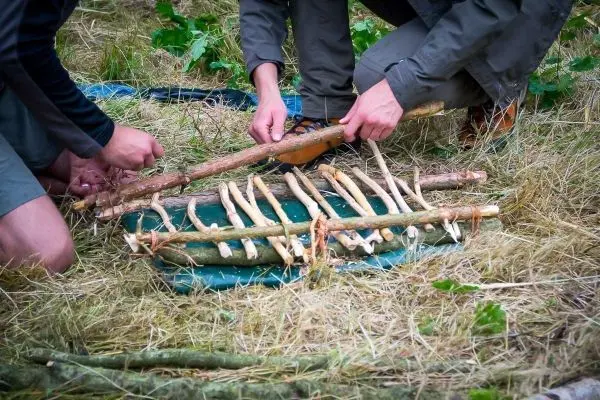 Zwei Personen bauen eine Holzstruktur aus Ästen auf einer grünen Unterlage